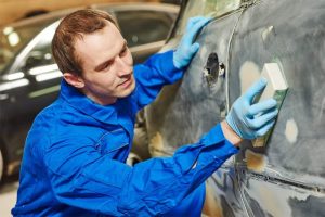 A painter sanding a car body but Do I Need to Sand Primer Before Painting a Car?